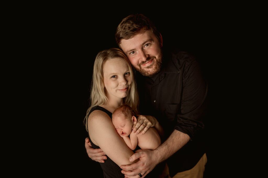 Black backdrop with photo of mom holding baby and dad embracing them both 