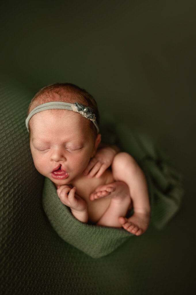 Baby girl wrapped in green wrap posed on a matching green backdrop during her newborn session.