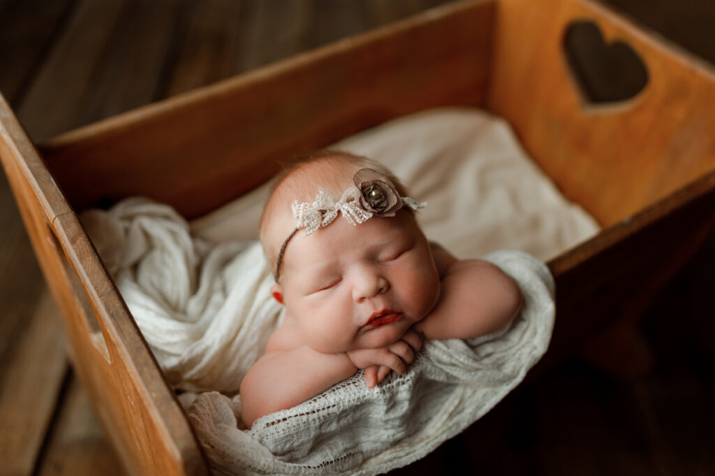 baby girl posed in a crib with her hands under her chin. 