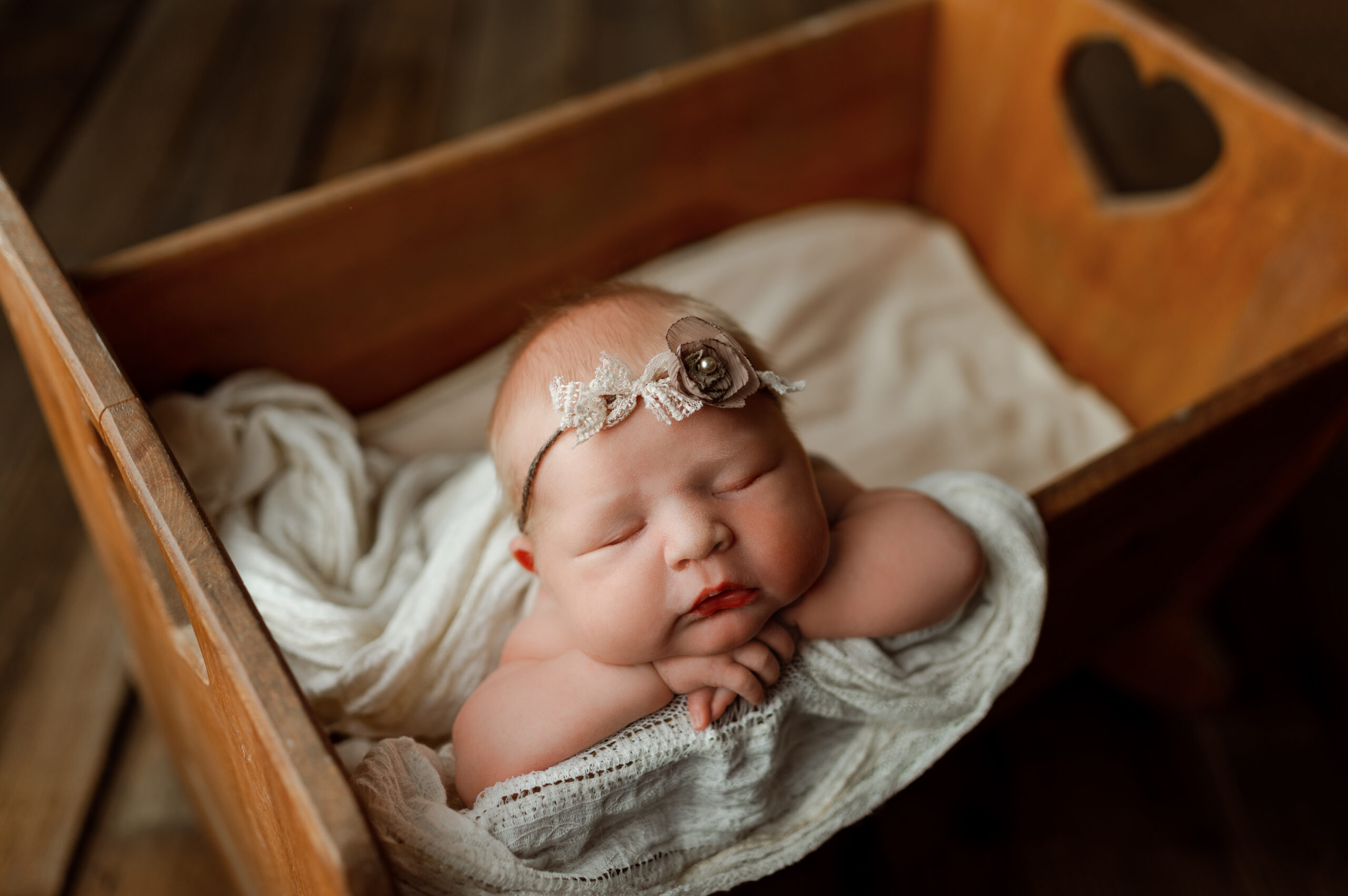 newborn baby girl posed in a wooden crib with a heart shape cutout