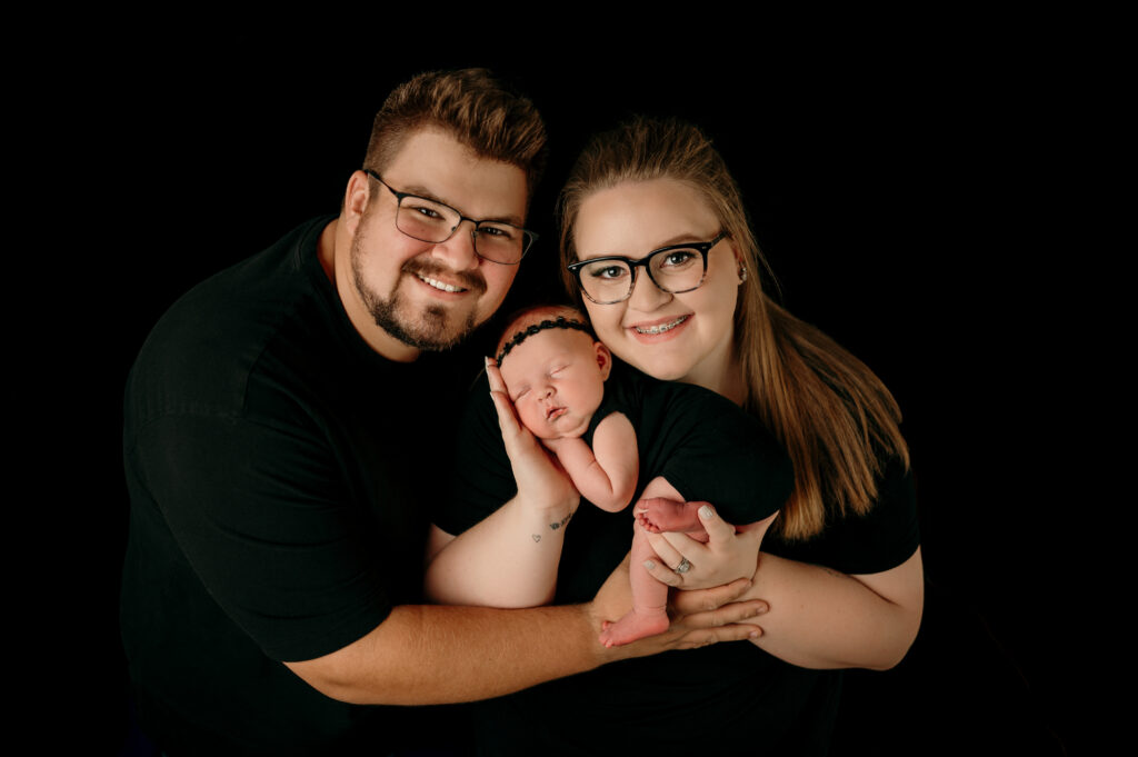 mom, dad, and newborn baby posed on black backdrop 