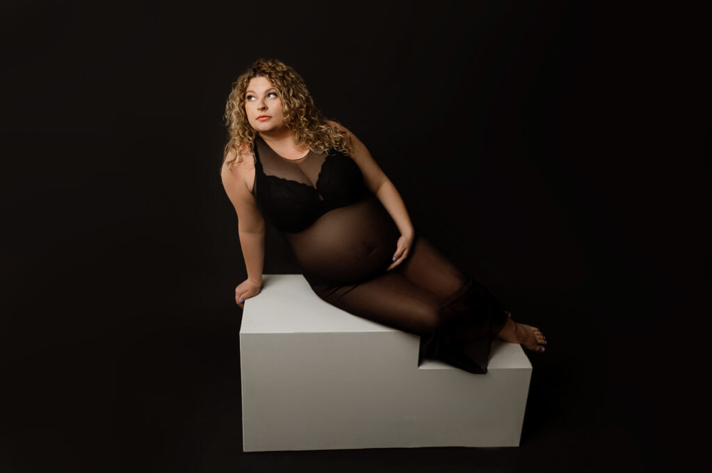 a pregnant mother wearing a sheer black dress posed on white blocked for a studio style maternity photo