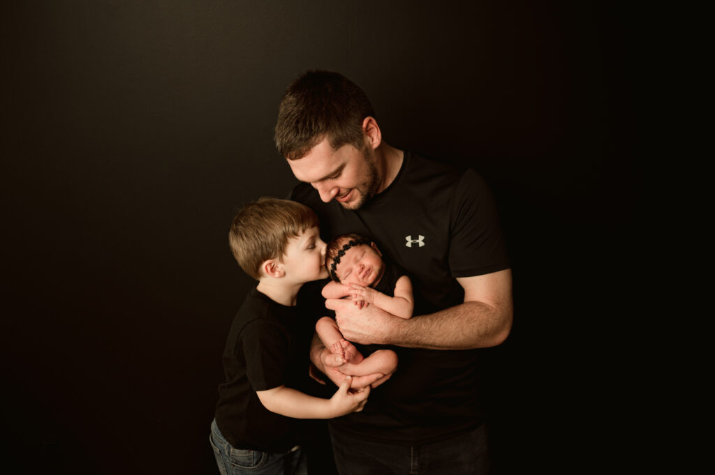 family of four with a newborn girl being photographed in a studio session