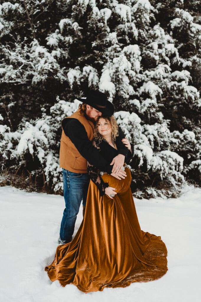 A couple dressed in western style clothes doing maternity photos in the snow in St Joseph