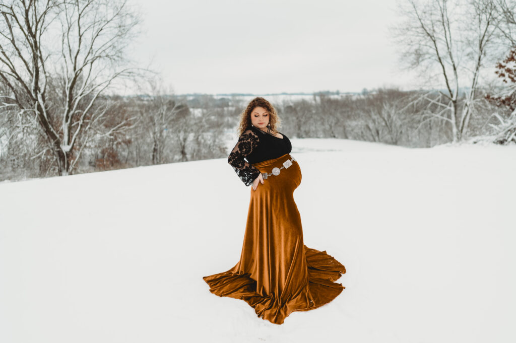 a mom in a velvet skirt and western lace top posing for maternity photos in the snow