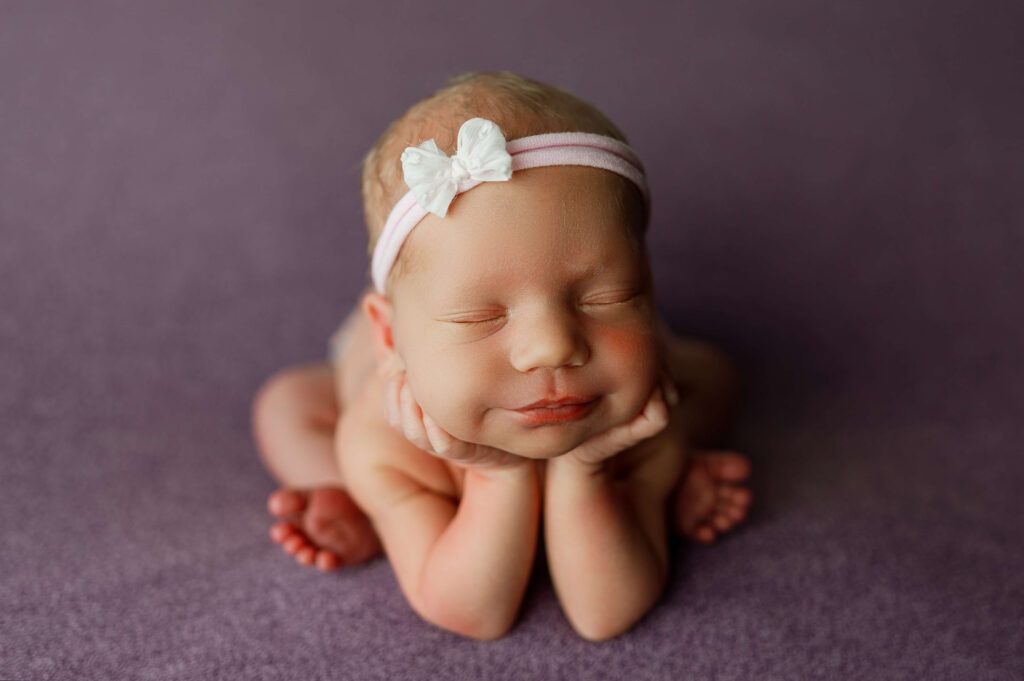 baby girl posed in newborn "froggy" pose on purple backdrop.
