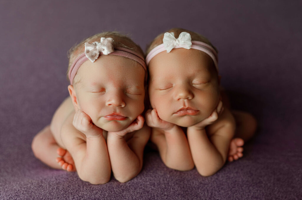 twin baby girls posed in newborn "froggy" pose on purple backdrop.