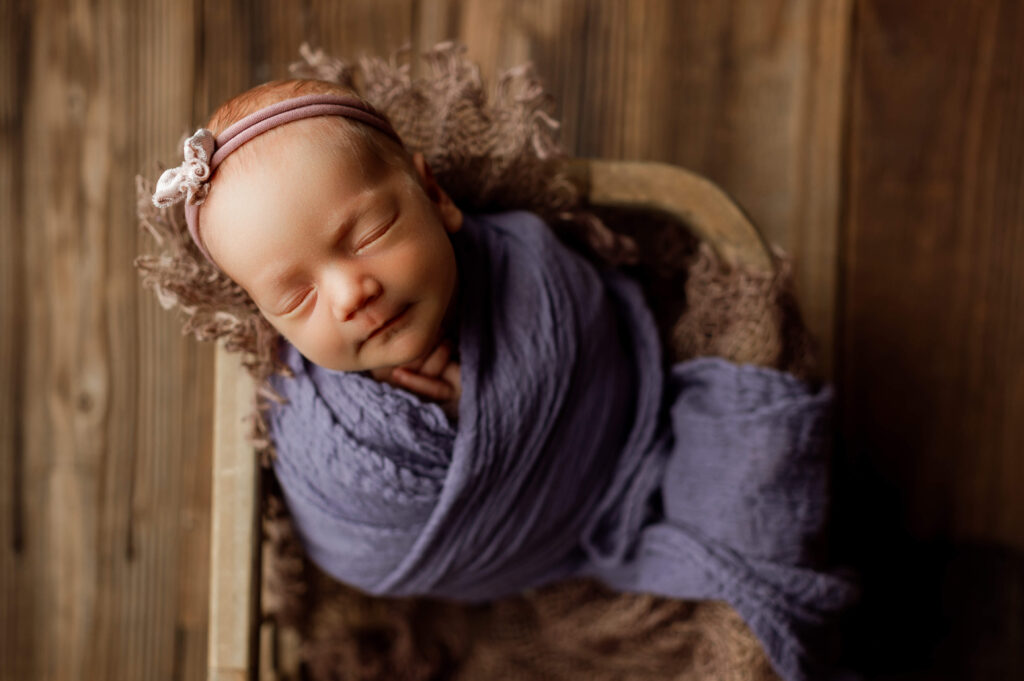 baby girl wrapped in purple place in a basket posed specifically for newborn photograhy