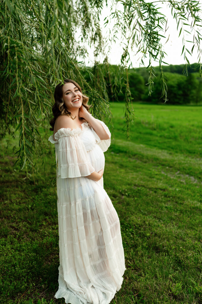 a pregnant mother posed under a willow tree in a flowy white dress
