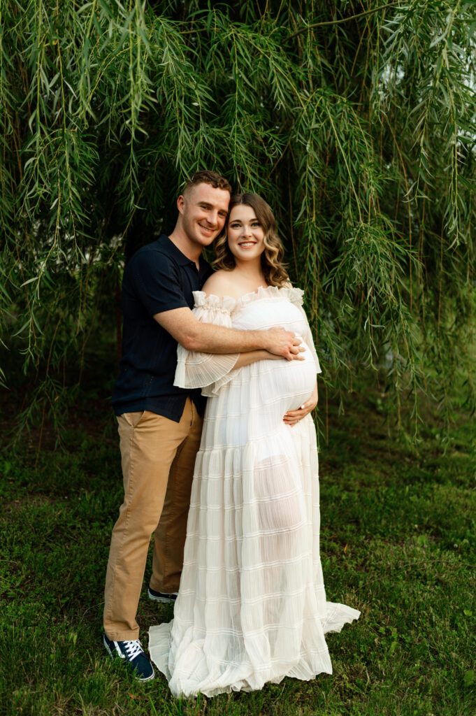 a couple posed for maternity pictures under a willow tree